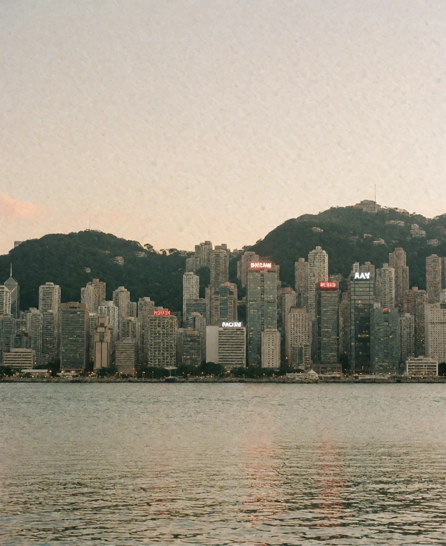 Hong Kong harbour skyline at soft dusk seen from the waterfront with green hills behind