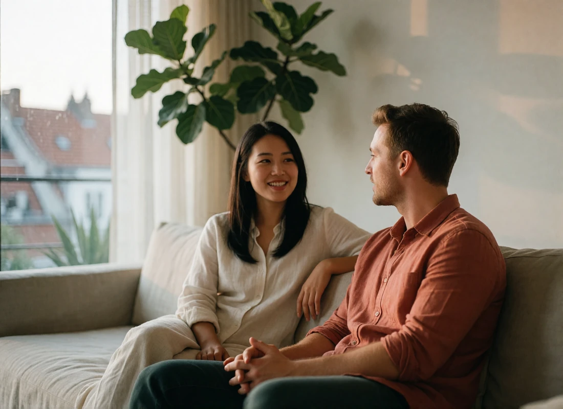 Asian woman and Western man sitting close together on a linen sofa in a bright modern apartment, mid-conversation